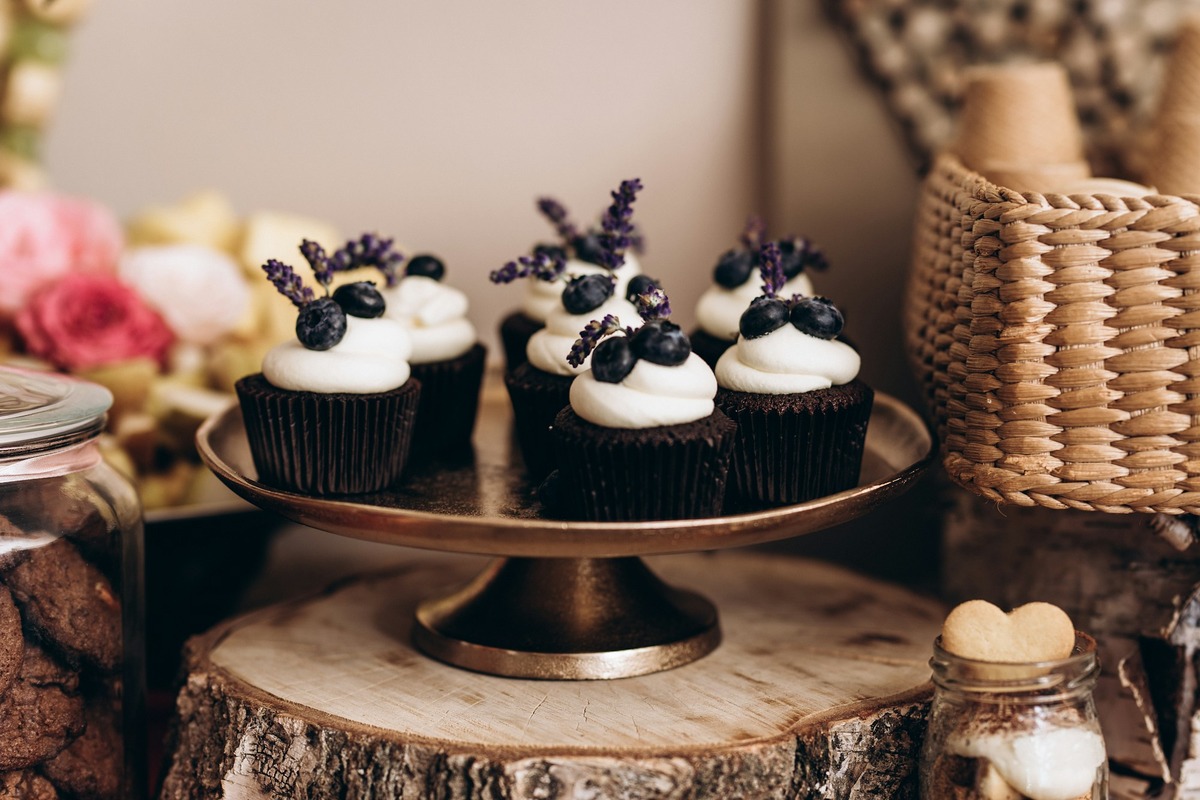 Assorted cupcakes with white frosting, blueberries, and lavender on a gold stand