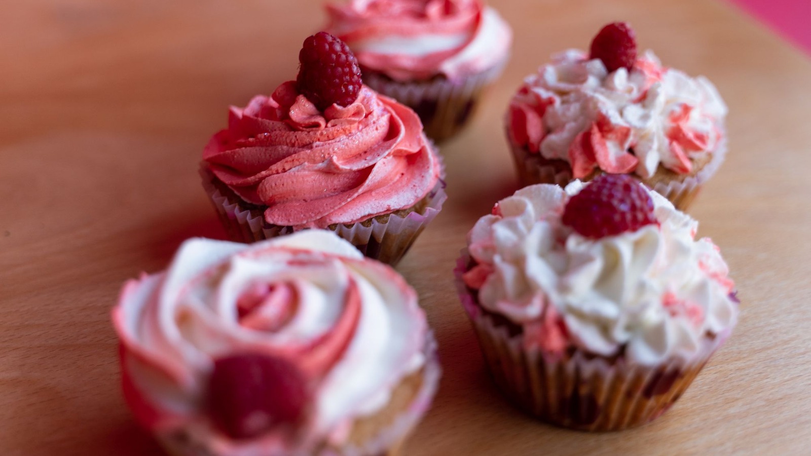Pink raspberry cupcakes with white frosting on a wooden board